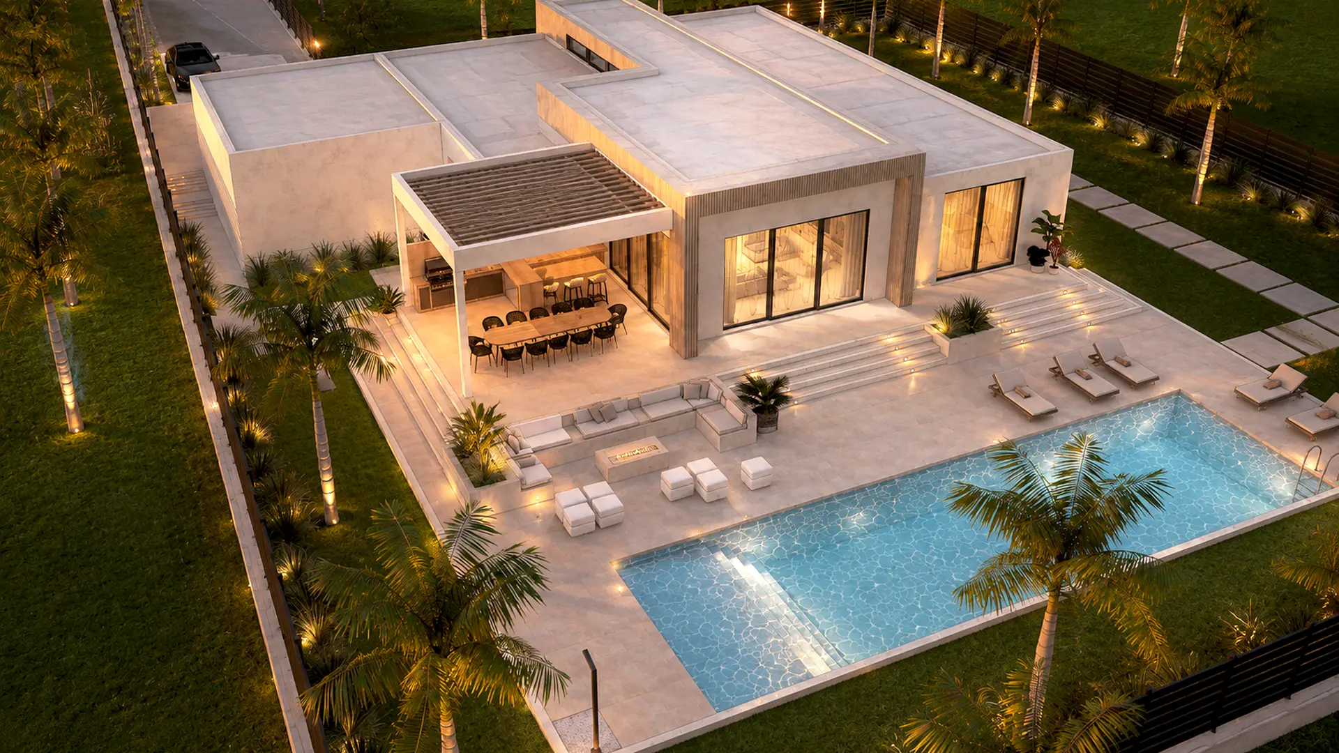 Aerial view at dusk: the flat-roofed villa upper-left, the pergola and lounge mid-frame, the lit pool lower-right